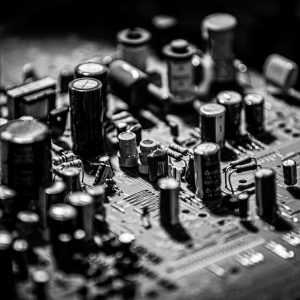 Grayscale close-up of electronic circuit board with capacitors and transistors.